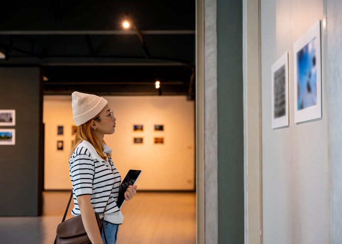 Young person at photo frame hold digital book leaning against at show exhibit artwork gallery Young person at photo frame hold digital book leaning against at show exhibit artwork gallery, Asian woman holding tablet at art gallery collection in front framed paintings looking pictures on wall